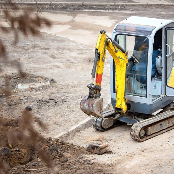 Tracked mini excavator breaks out old curbs before installing new curbs. The concept of using economical and compact equipment for urban needs.